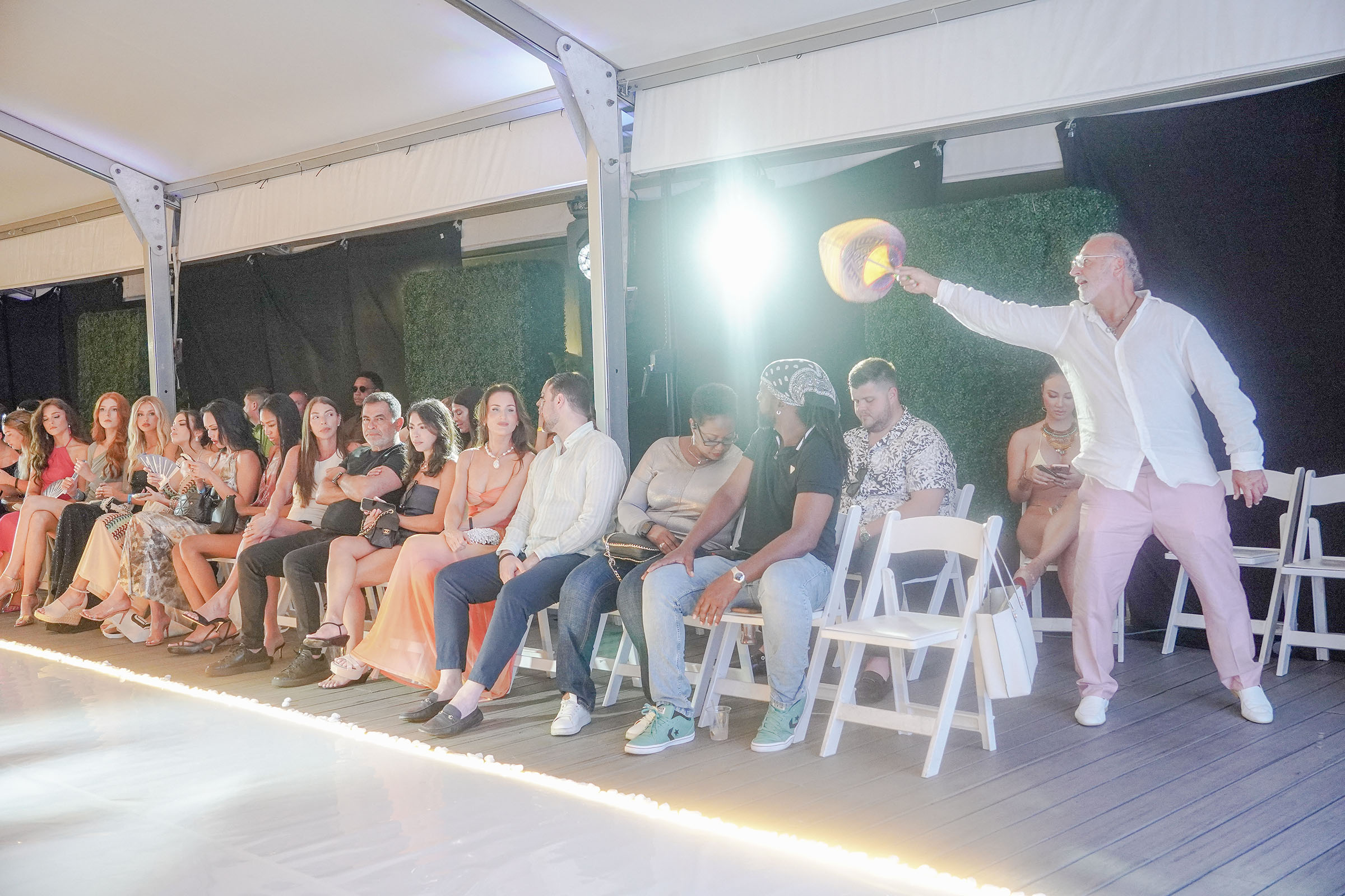 A guest waves a fan beside the runway while the audience waits for the next look.